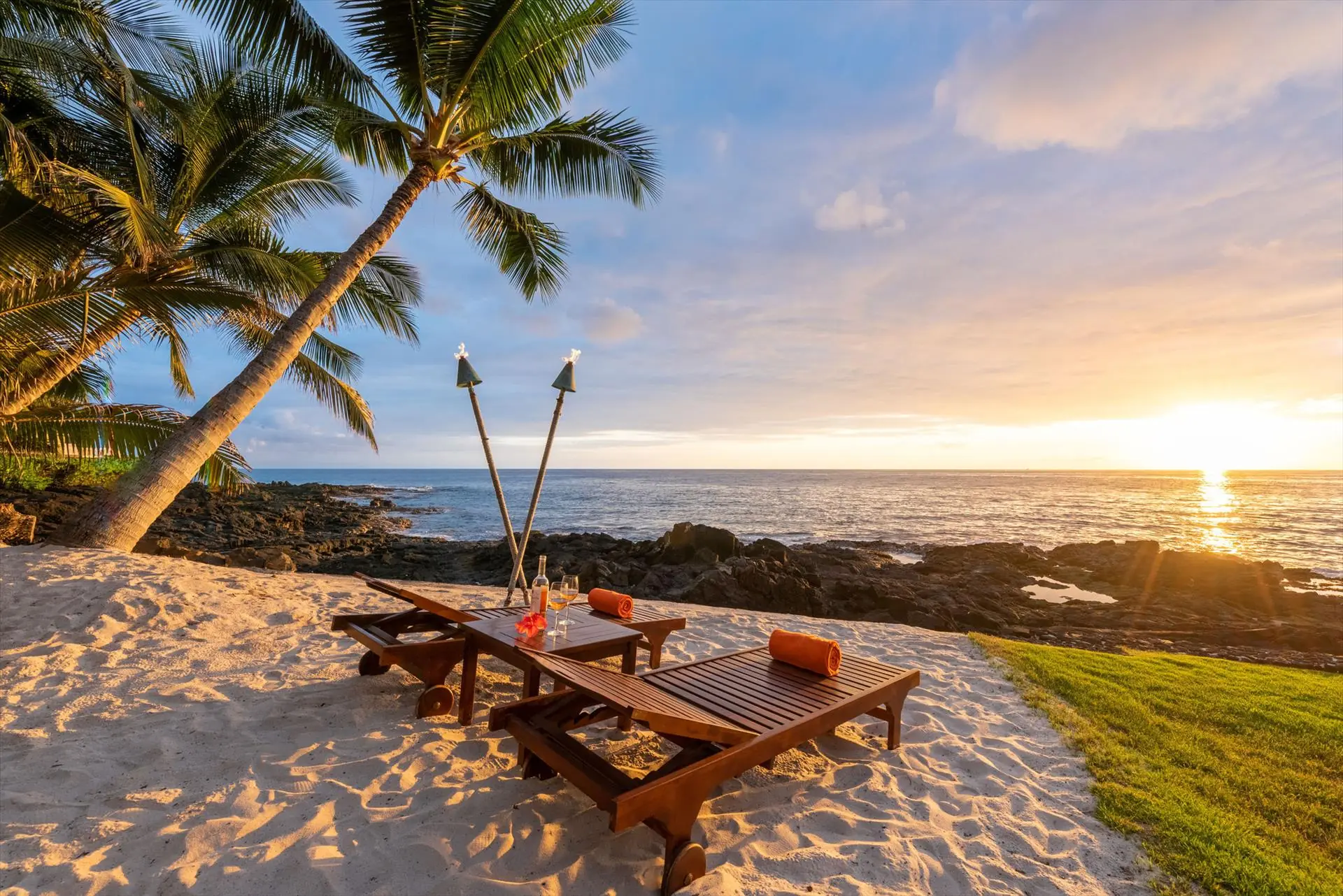 Sunset over the lava shoreline with tiki torches and loungers